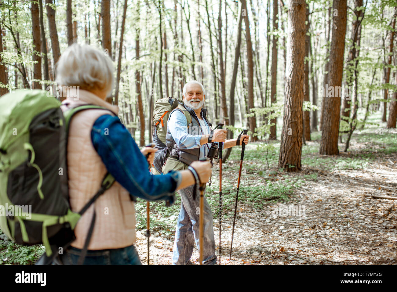 Beautiful senior couple hiking with backpacks and trekking sticks in the forest. Concept of active lifestyle on retirement Stock Photo