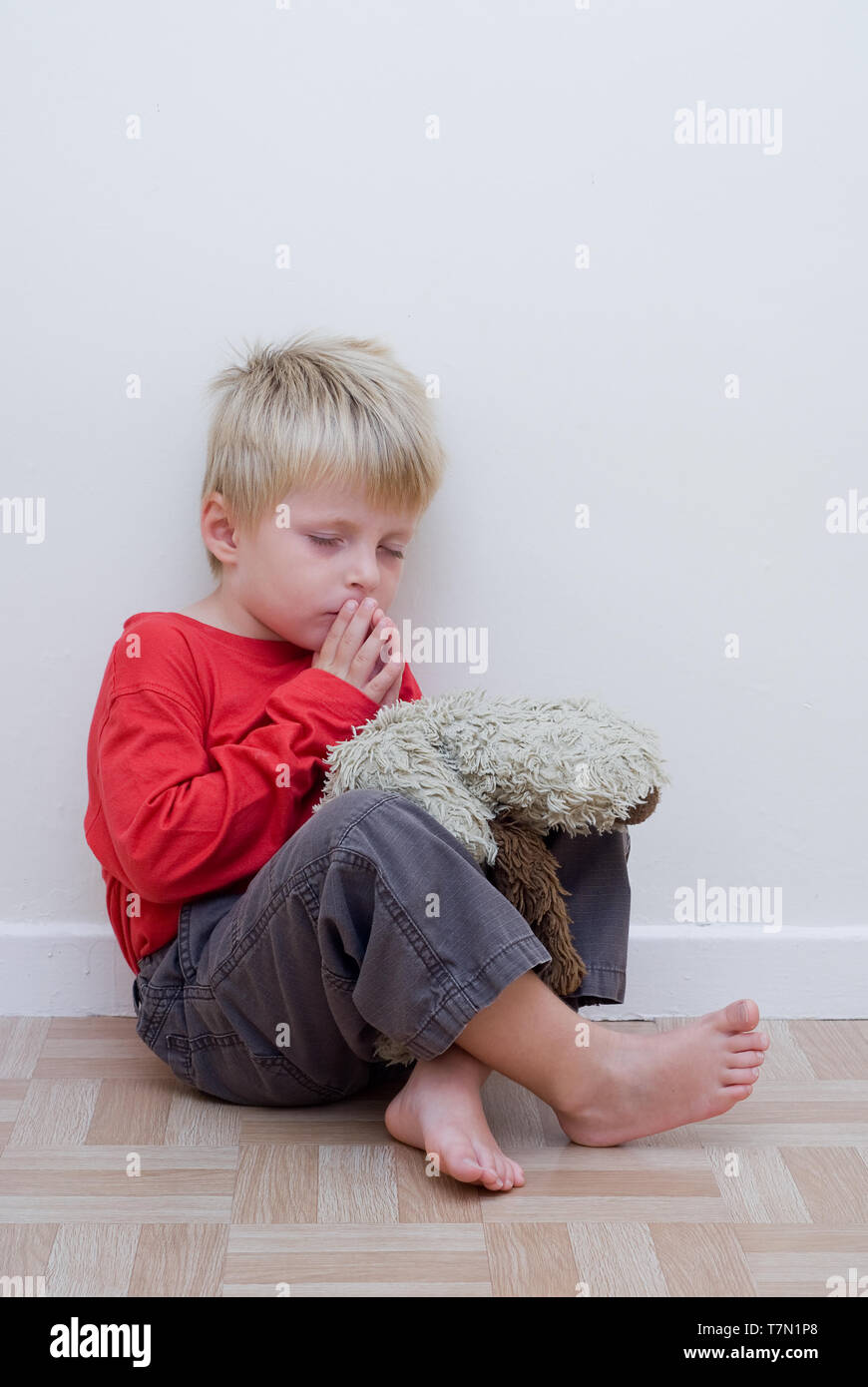 Little boy sitting on the floor and praying with his toy dog next to him. Stock Photo