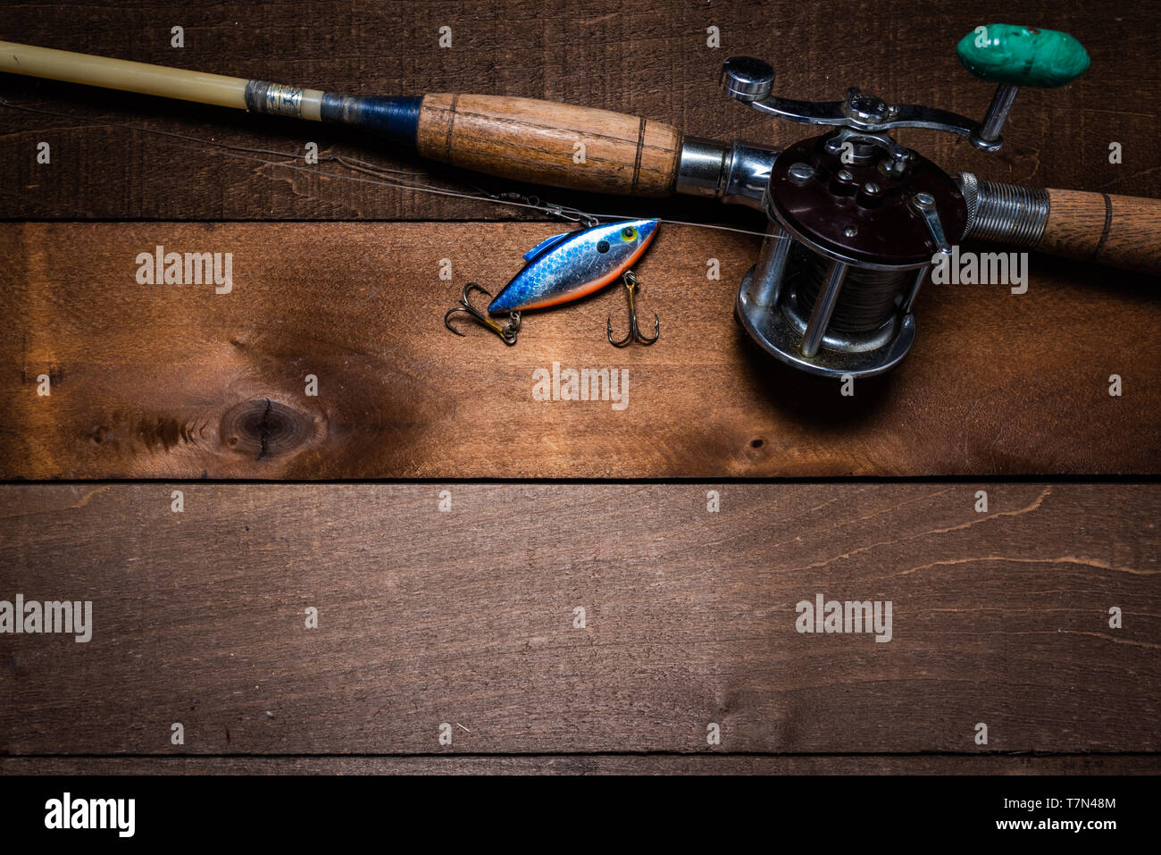 A vintage fishing rod and reel, with a lure on a wooden plank background  with copy space Stock Photo - Alamy