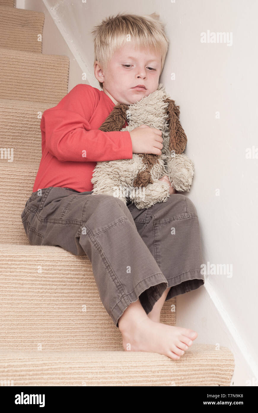Lonely child sitting on the stairs, hugging his soft toy. Stock Photo