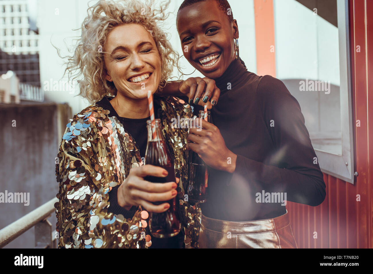 Happy young women with soft drinks standing together outdoors. Two female friends having a great time on weekend. Stock Photo