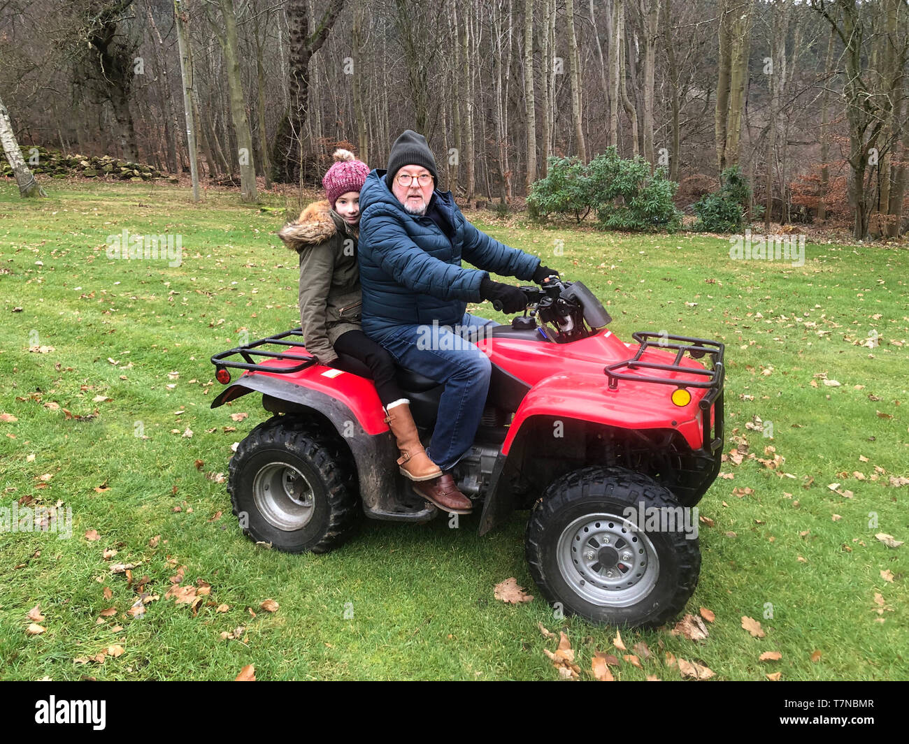 Litle girl is riding on a quad with her father, they are both looking at the camera. Stock Photo