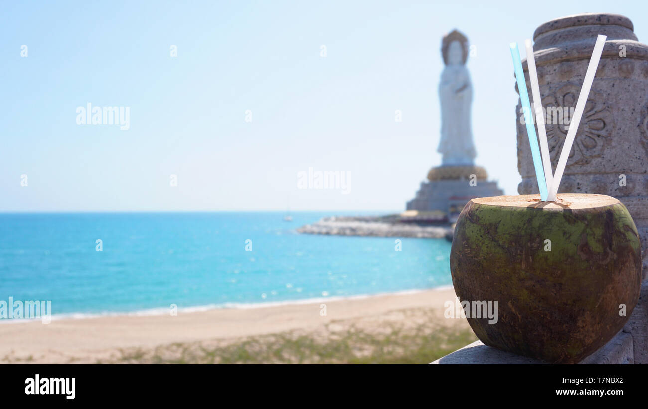 Guanyin of Nanshan, the white statue of the bodhisattva Guanyi near the Nanshan Temple of Sanya, China. In the foreground a coconut cocktail, the sea Stock Photo