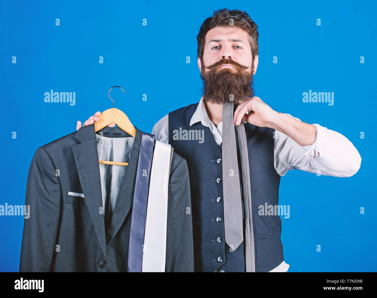 How about this tie. Brutal hipster holding colorful tie collection and suit jacket. Bearded man matching neck tie color to formal coat. Choosing a perfect tie. Stock Photo