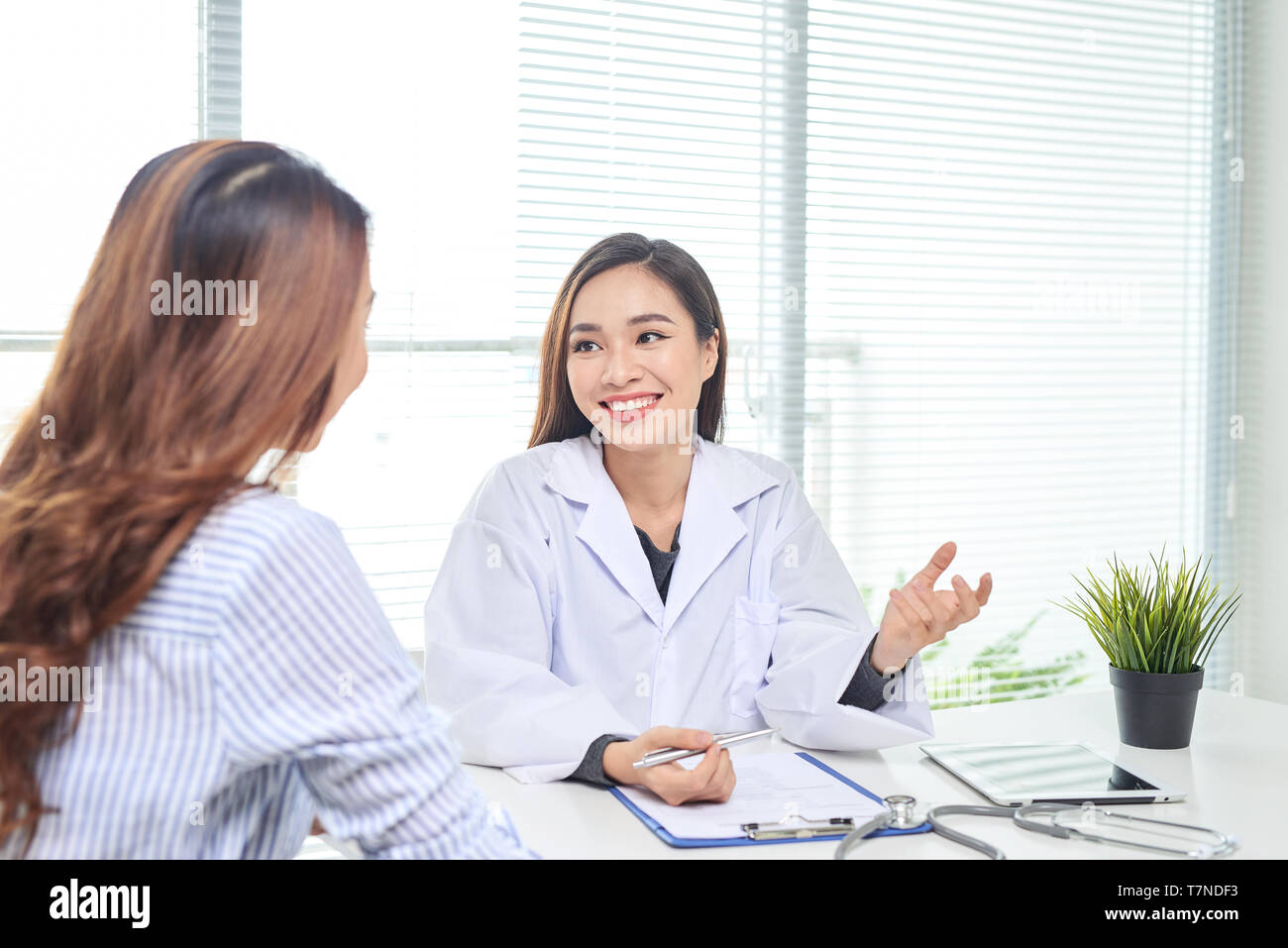 Female doctor talks to female patient in hospital office while writing ...