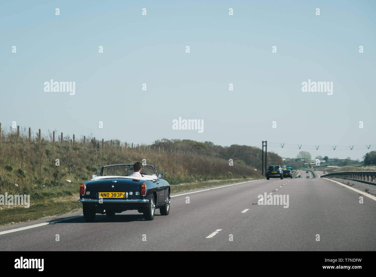 Norfolk, UK - April 21, 2019: Man driving a retro convertible car with the hood down on A11, a major trunk road in England that runs roughly north eas Stock Photo