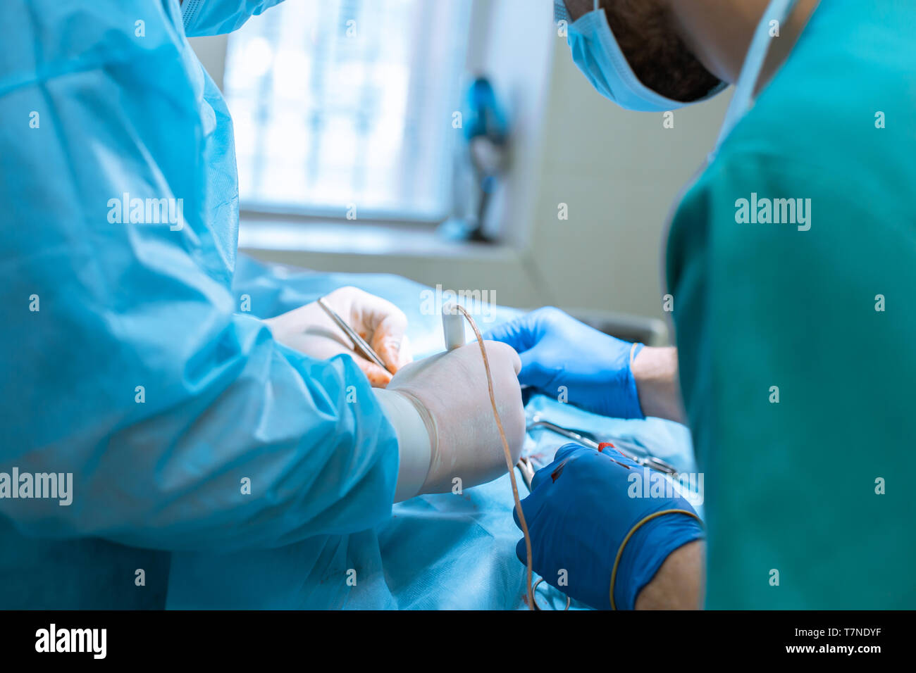 A male surgeon in a mask and gown operates in a sterile operating room with an assistant and an anesthesiologist. The medical team performs the operat Stock Photo
