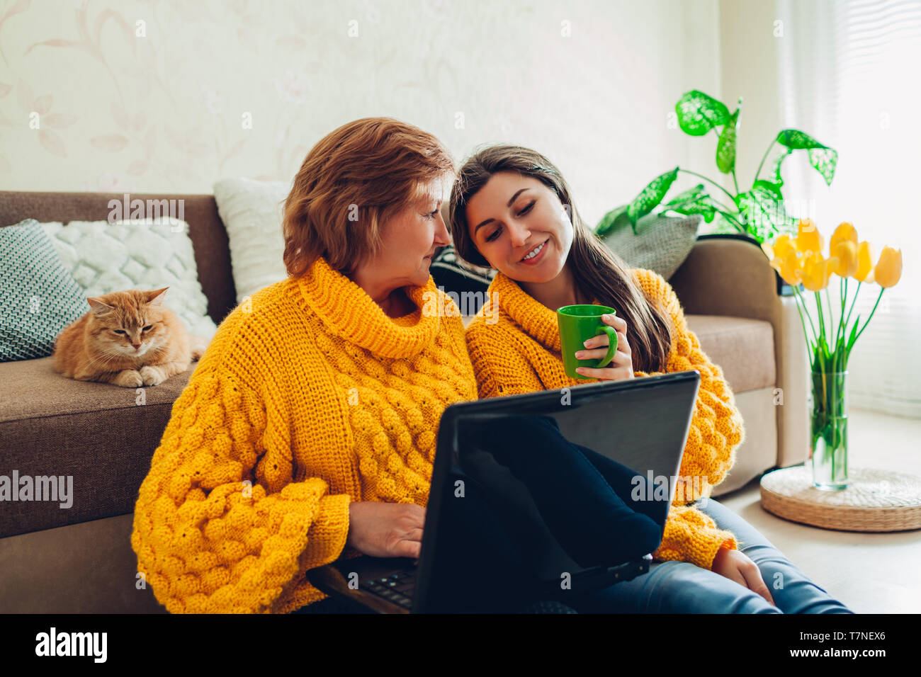 Senior mother and her adult daughter using laptop at home while drinking tea. Mother's day concept. Stock Photo