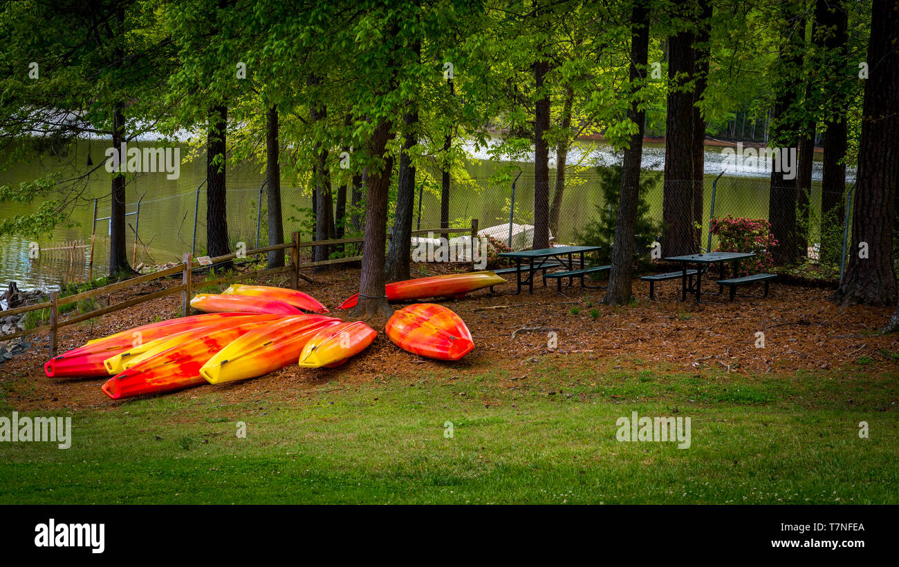Orange and yellow kayaks stored upside down on grass with lake in the background Stock Photo