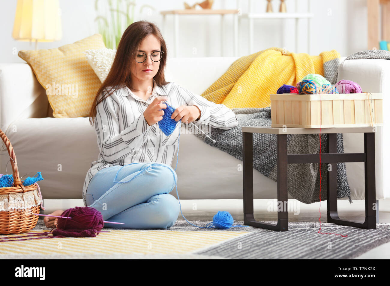Young woman sitting on carpet and knitting warm sweater at home Stock ...