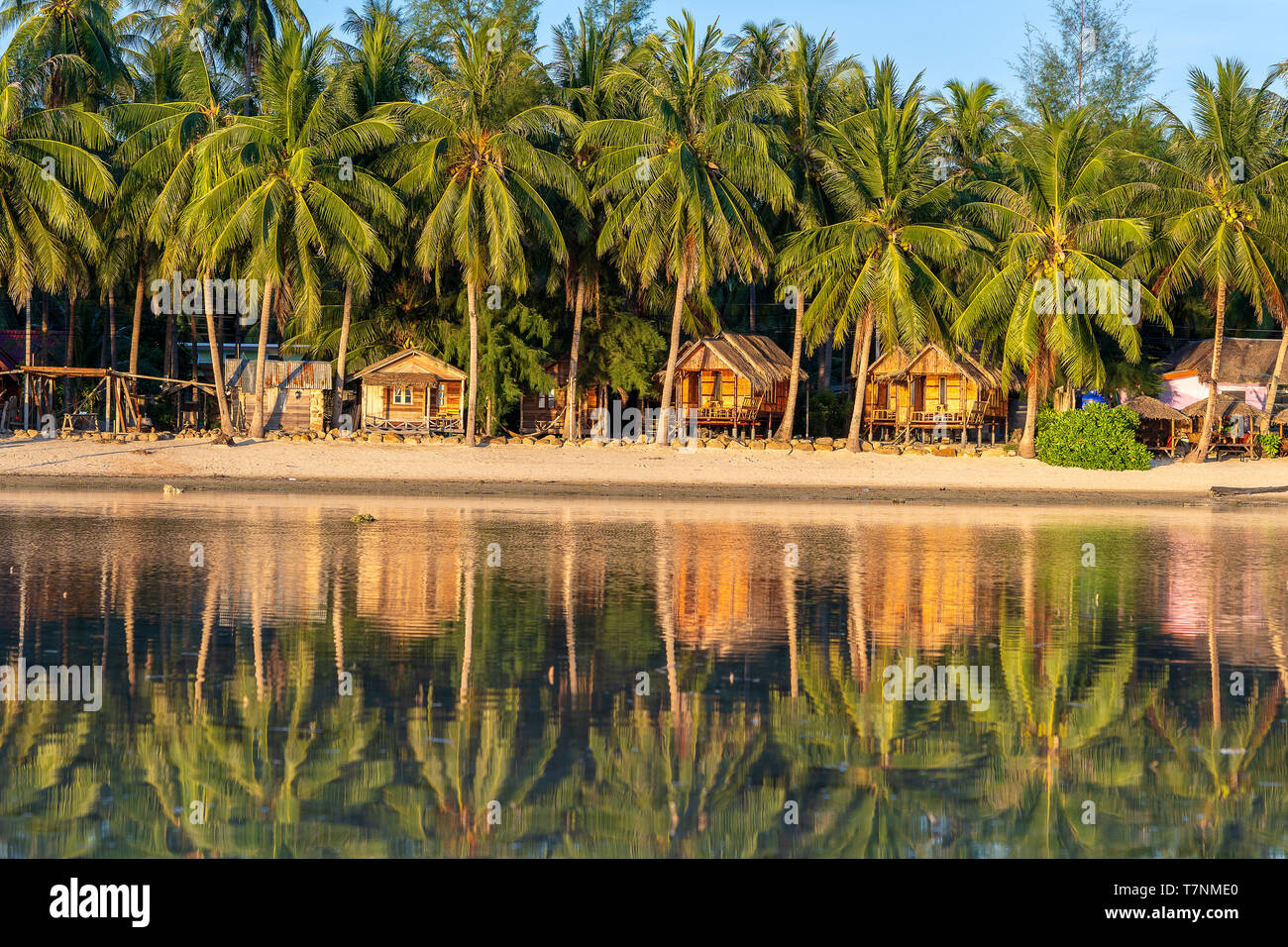 Beautiful bay with coconut palm trees and wooden bungalows which is reflected in seawater. Tropical sand beach, green palm leaf and sea water on the i Stock Photo