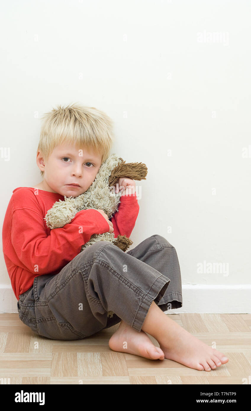 Lonely upset child sitting on the floor with his teddy bear. Stock Photo