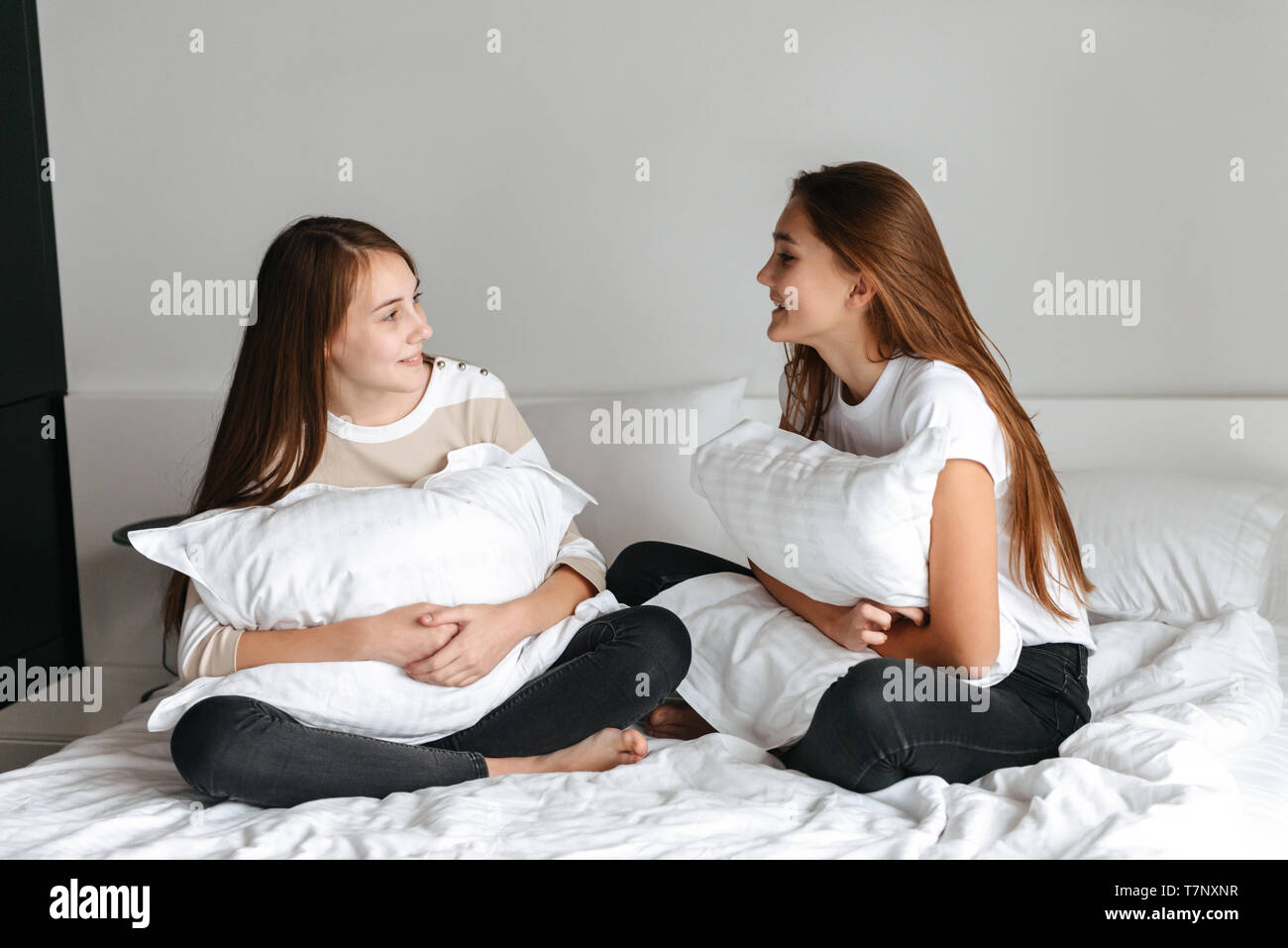 Two cheerful young teenage girls talking while sitting on bed at home
