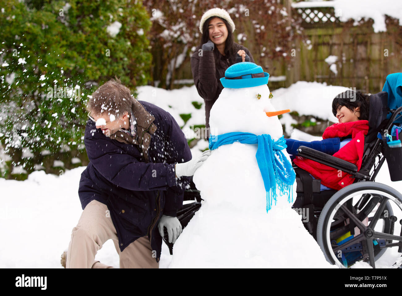 Caucasian father having fun  playing snowball fight with biracial children outdoors in winter. Young boy is disabled in wheelchair. Stock Photo