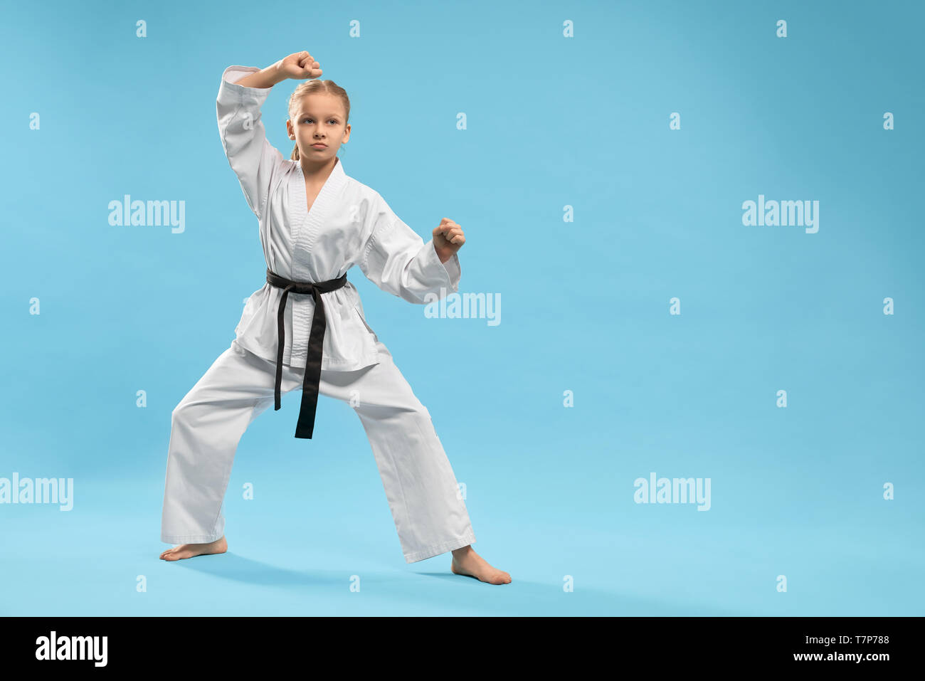 Angry female fighter in white kimono practising karate and jujitsu on blue isolated background