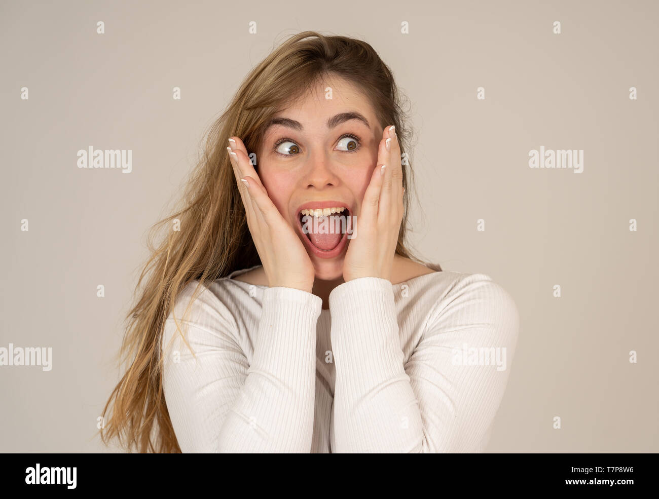 Beautiful young blonde teenager woman with happy face making surprised gestures looking and pointing at something shocking and good. Human facial expr Stock Photo