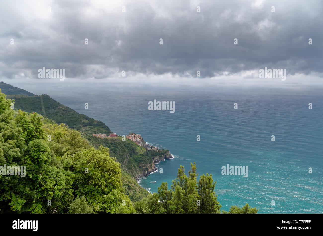 Looking down to a distant Manarola from high up on the Cinque Terre trail as grey clouds roll in over the sea Stock Photo