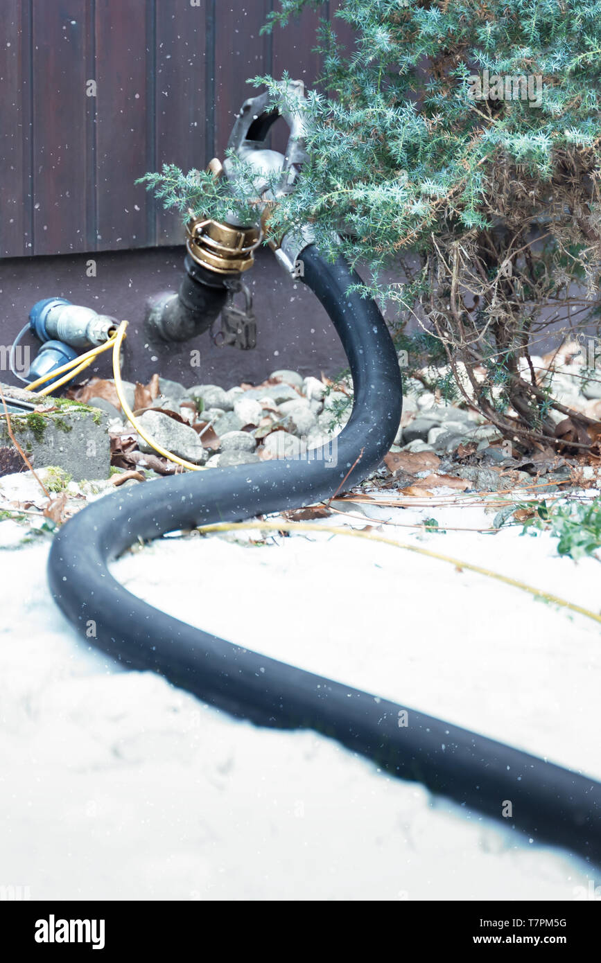 In the snowy garden you can see a hose. Heating oil is supplied in the hose. The hose carries the oil into the tank in the house for heating. For a co Stock Photo