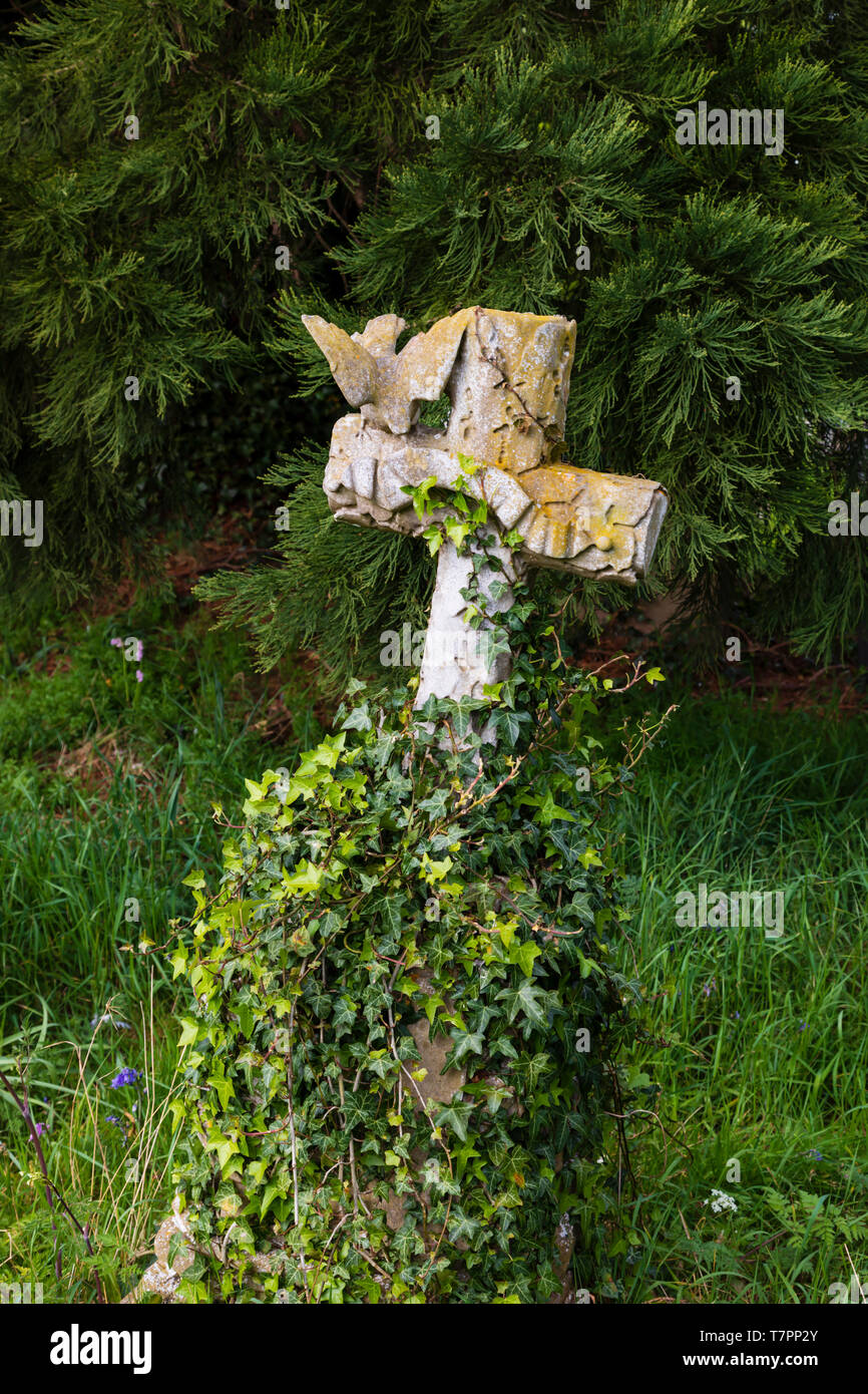 Grave cross overgrown in St Peters Chuch graveyard, in the village of Dunchurch, Warwickshire, West Midlands, England. The grass is being left to grow Stock Photo