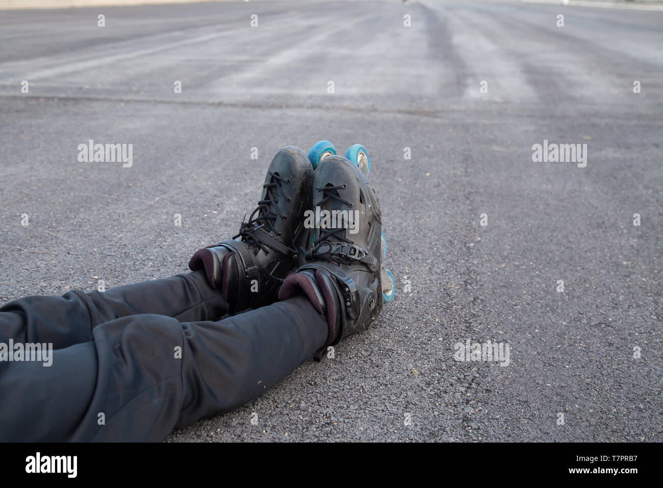 Crop from above young tired fit man in sportswear with roller skates lying on road and relaxing Stock Photo