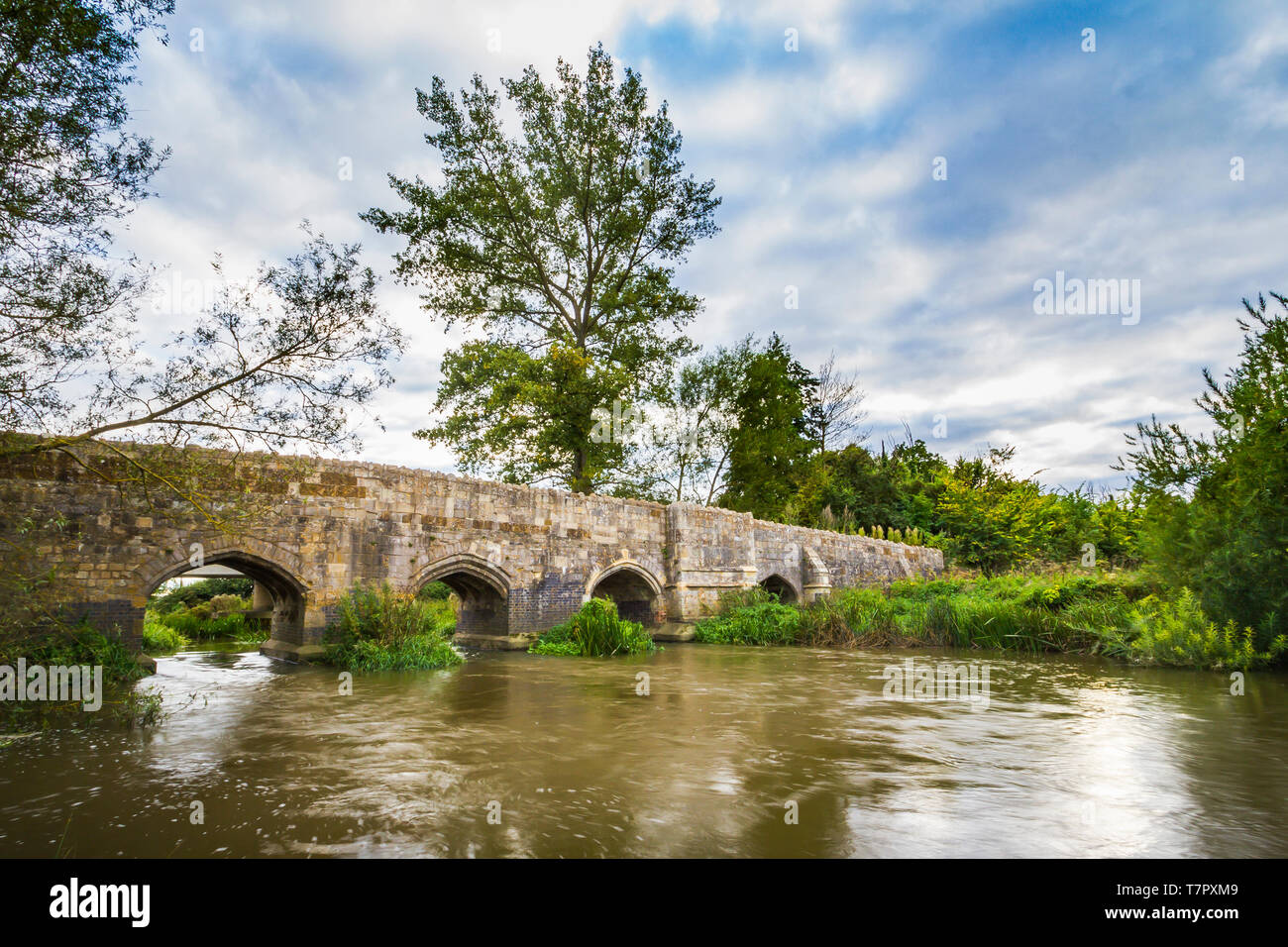 Old stone medival bridge over a streaming river in England. Dramatic cloudscape and old color tones Stock Photo