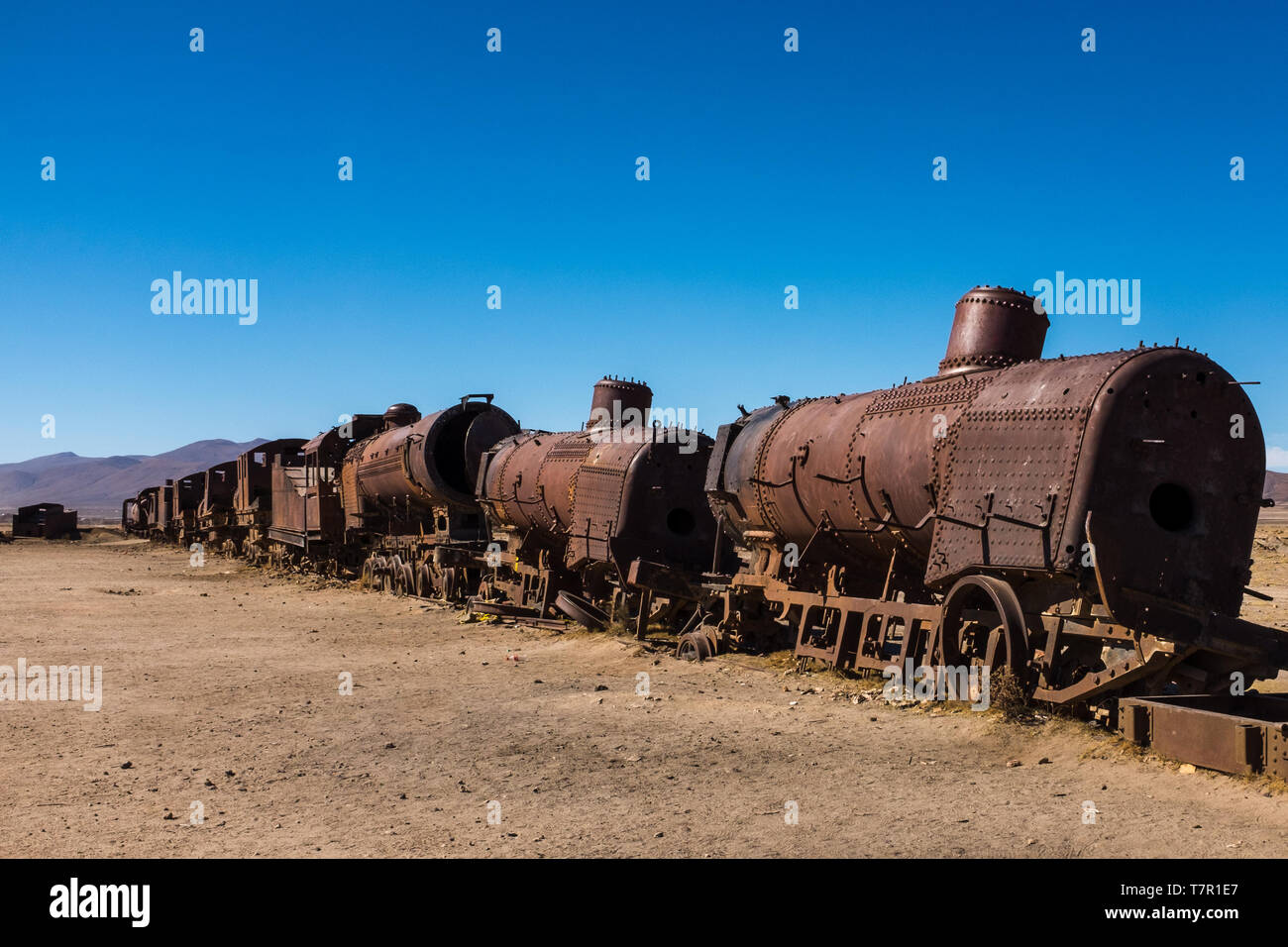 Rusting steam trains and carriages slowly rot away at the train graveyard just outside of Uyuni, Bolivia, against a bright blue sky. Stock Photo