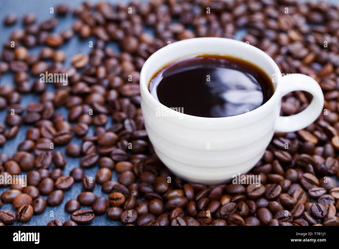 Black coffee in a white cup on freshly roasted coffee beans background. Close up. Stock Photo