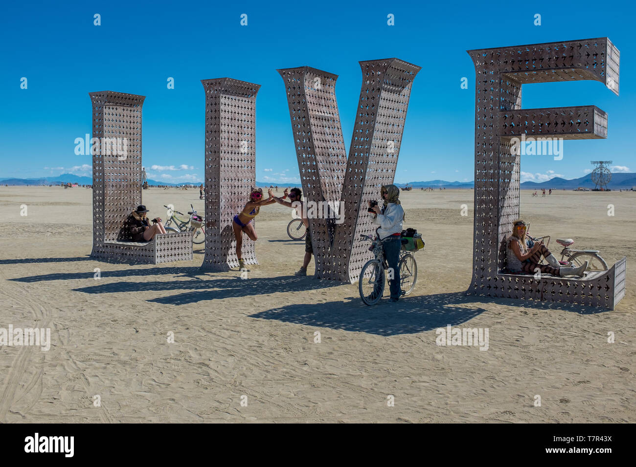 Burning Man, Nevada, USA, September, 6, 2015: Attendees at Burning Man festival sitting on and around an artwork of letters that spell out the word, LIVE against a bright blue sky. Stock Photo