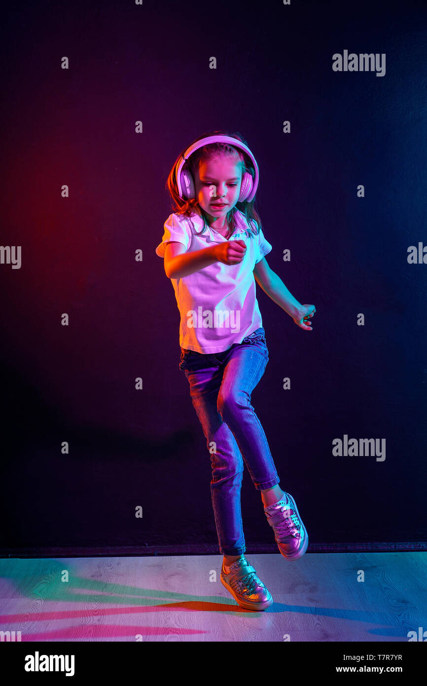 Girl of 7 years old listening to music in headphones and jump on dark
