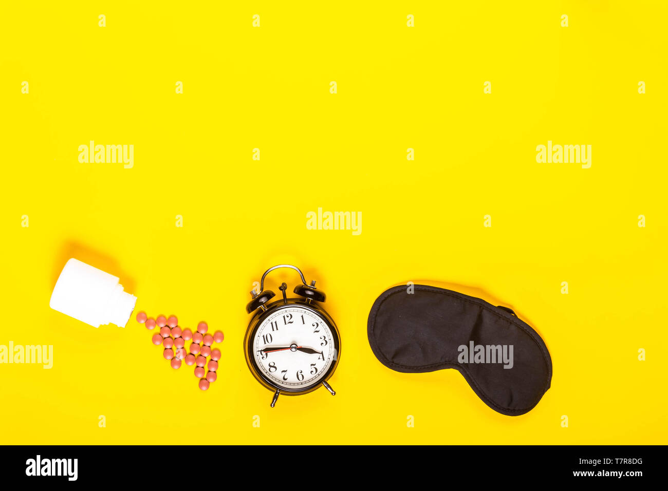 Sleep concept showing an eye mask, alarm clock and sleeping pills on a