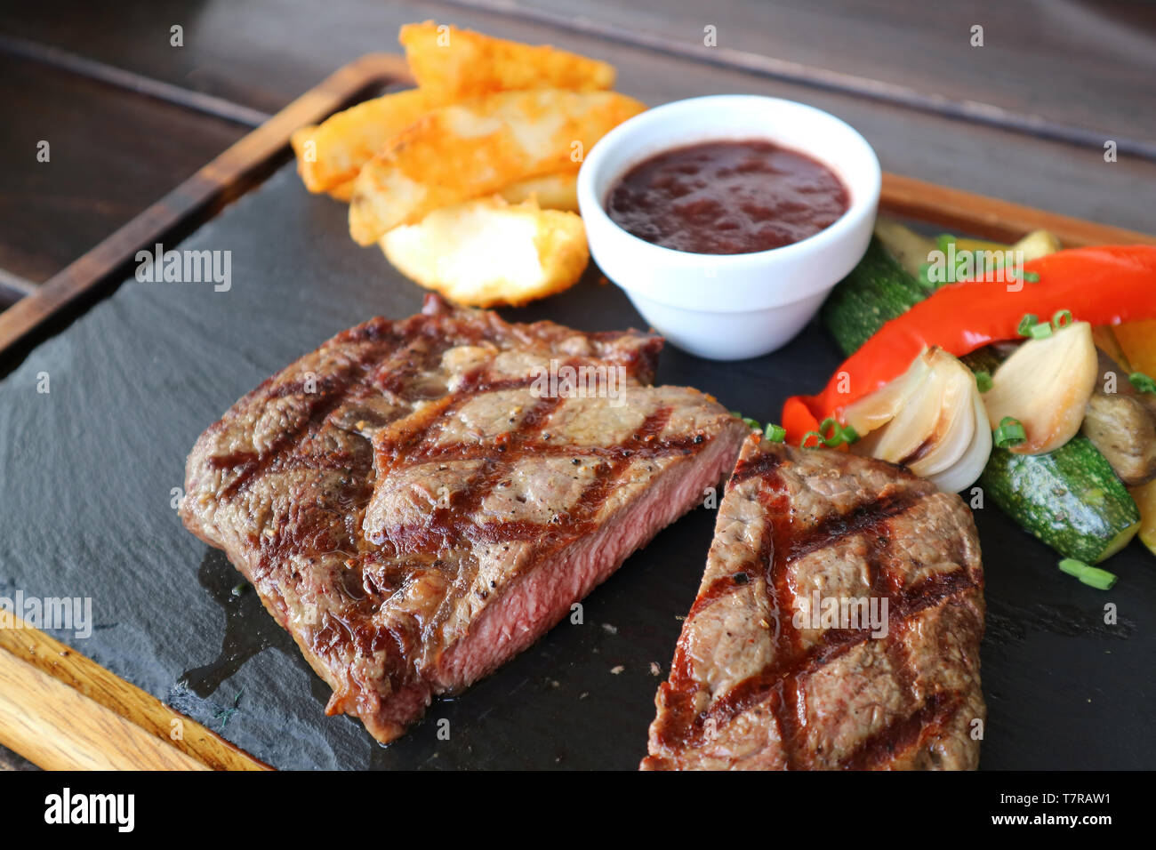 Cut medium grilled ribeye steak with red wine sauce and saute vegetables on hot stone plate