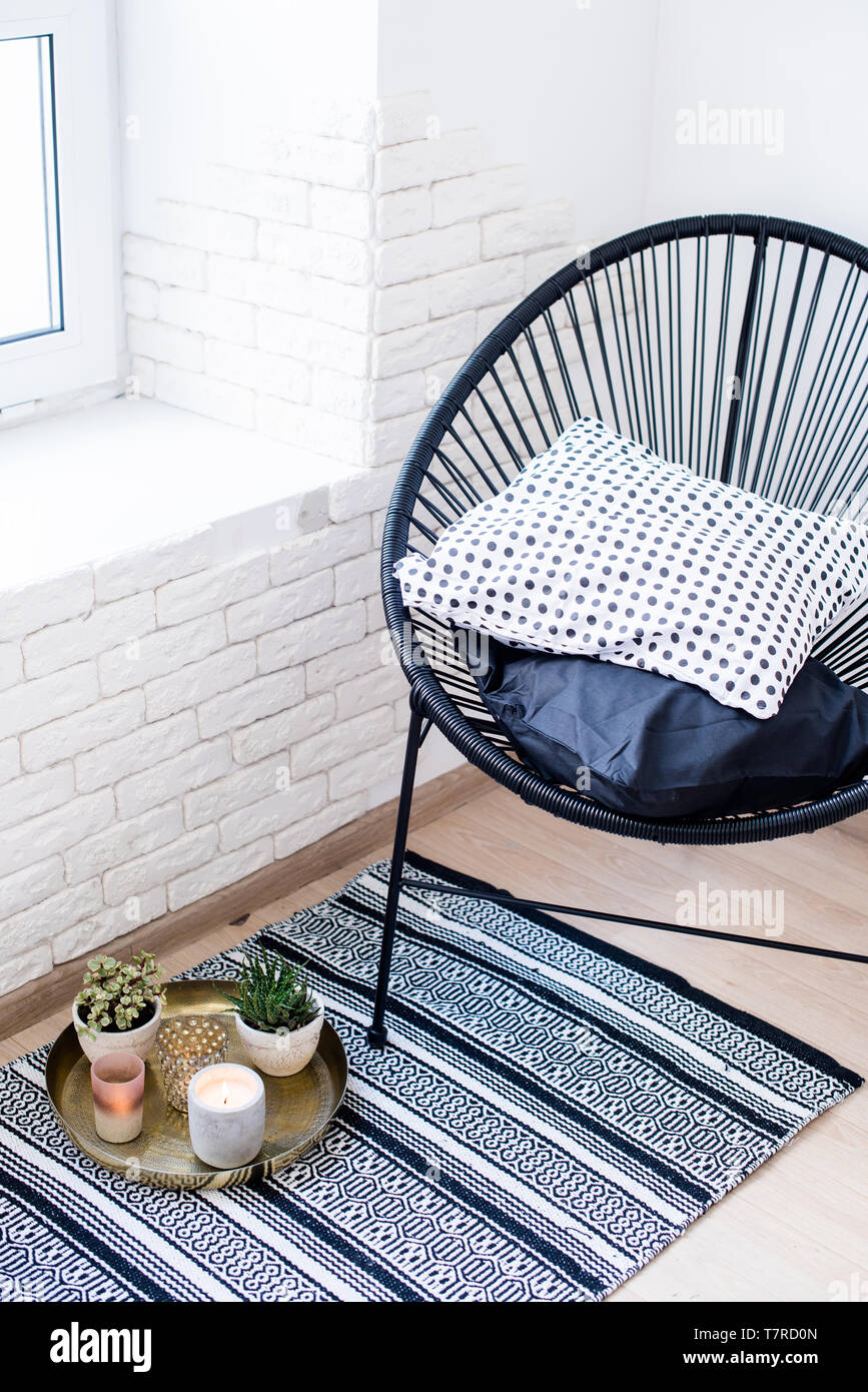 Bright white apartment interior decor, candles and plants on vintage tray with pillows in chair and carpet on the floor Stock Photo