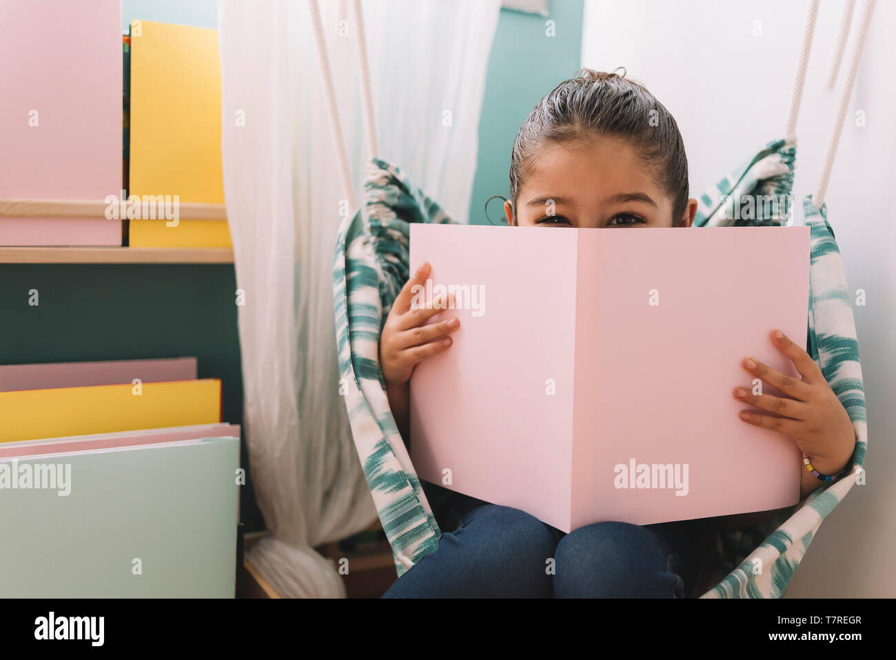 sweet happy little girl reading a book in her room near the window ...