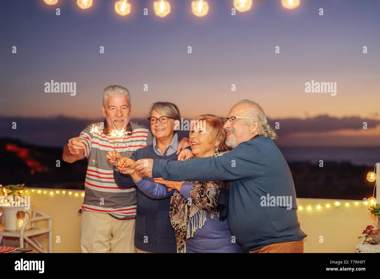 Happy senior friends celebrating birthday with sparklers stars outdoor - Older people having  fun in terrace in the summer nights Stock Photo