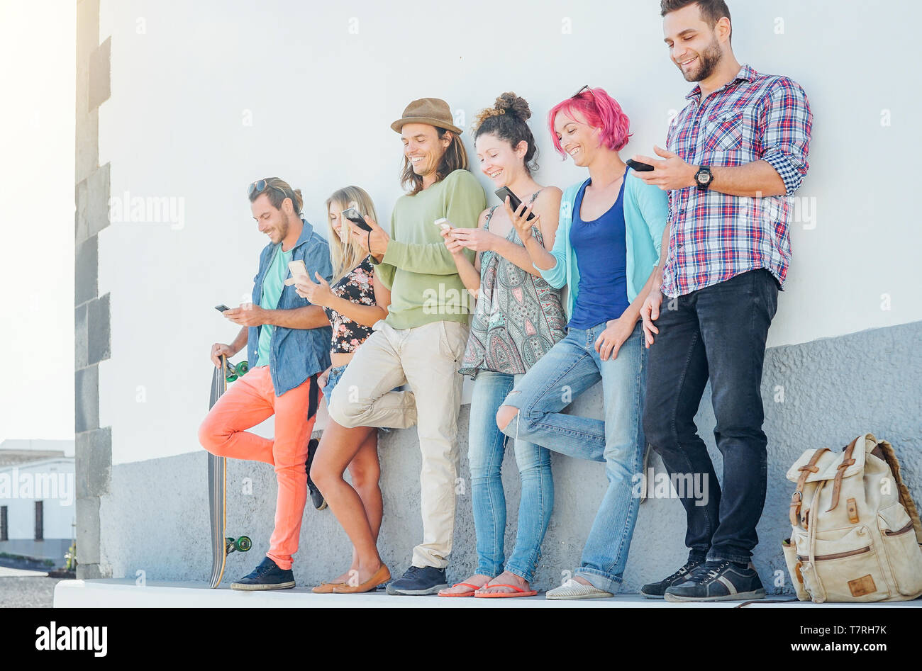Young people watching on their smart mobile phones leaning on a wall - Generation addicted to new technology Stock Photo