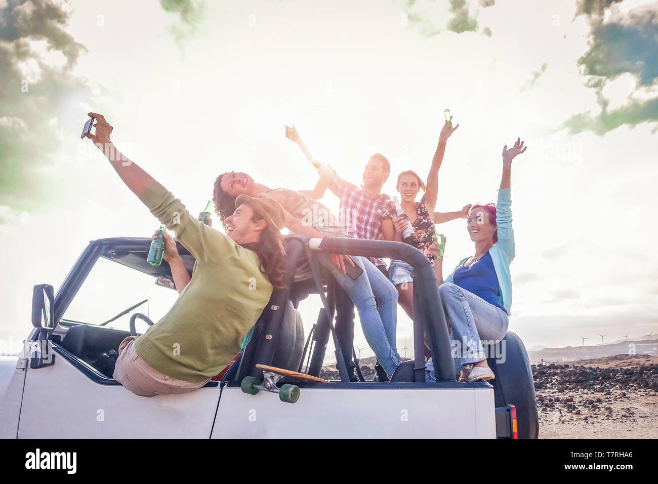 Group of happy friends having fun on convertible car in vacation - Young people drinking champagne and taking selfie during their road trip Stock Photo