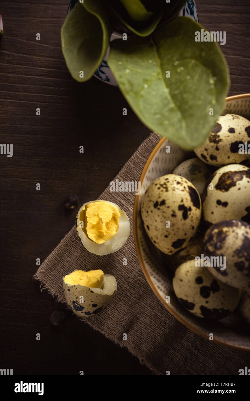 Vertical photo with top view on quail egg broken to two halves. Nice yolk with bright yellow color is inside. Bowl with next eggs is next to broken eg Stock Photo