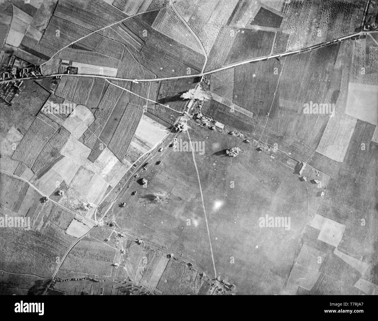 A contemporary British black and white photograph taken in 1917 from an aeroplane during the First World War. Photograph shows the bombing of a target in Northern France. A British aeroplane can be seen in small detail flying just over the road that runs left to right, having just dropped its bombs.  Aerial bombing World war One. Stock Photo