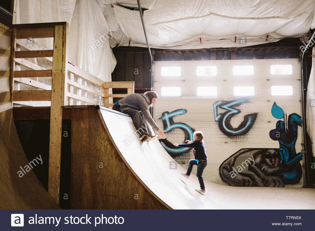 Father reaching for daughter on ramp at indoor skate park Stock Photo