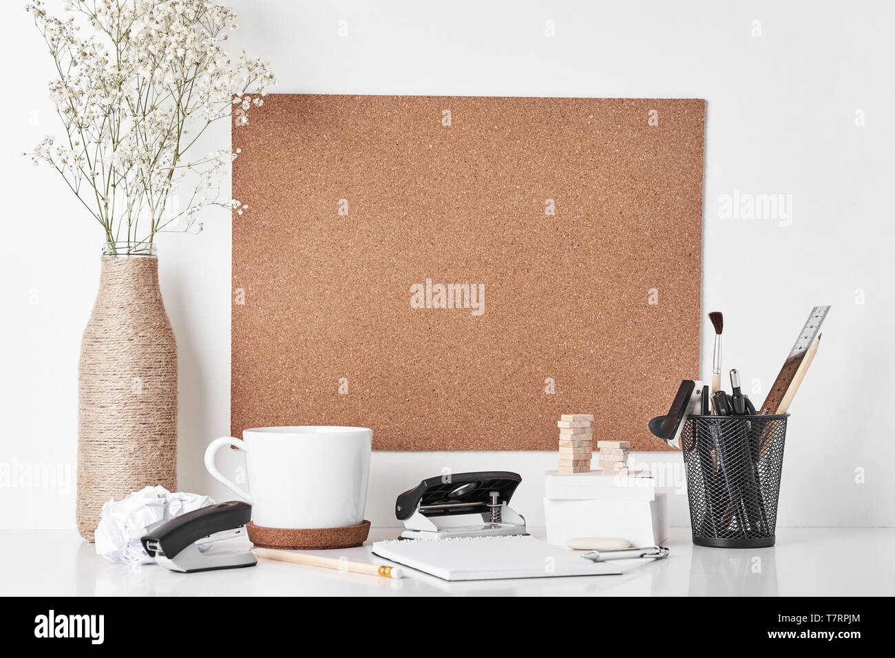 Cork board with office supplies, cup and plant in bottle vase on white