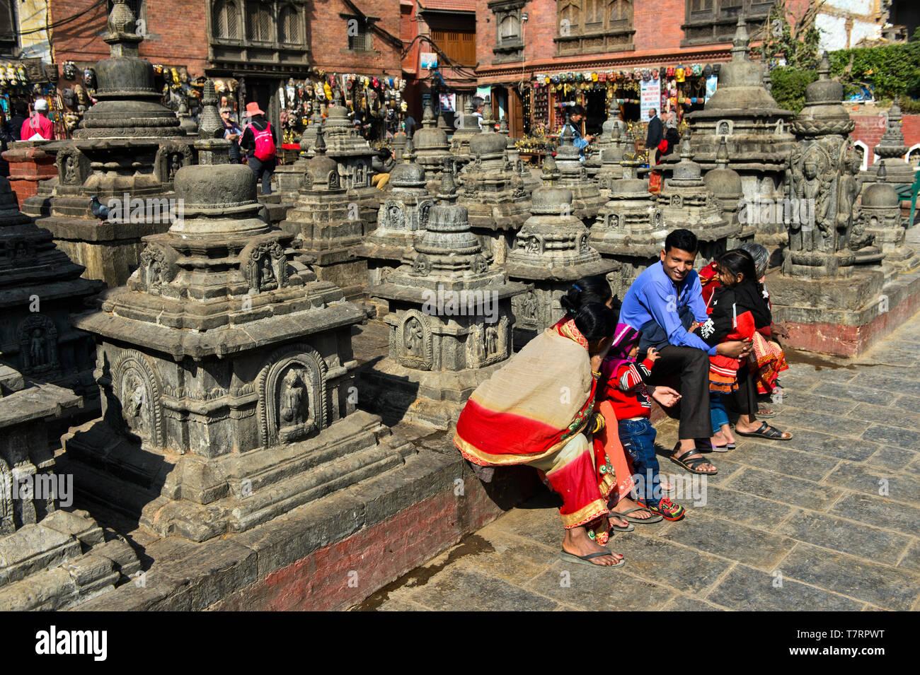 Local family in colorful dresses resting on a square with stupas on the site of the Swayambhunath temple or Monkey Temple, Kathmandu, Nepal Stock Photo