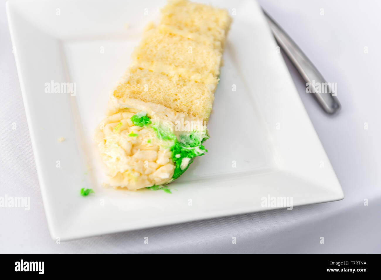 Restaurant or wedding reception white table tablecloth one plate with vanilla cream cake slice closeup and green food coloring Stock Photo