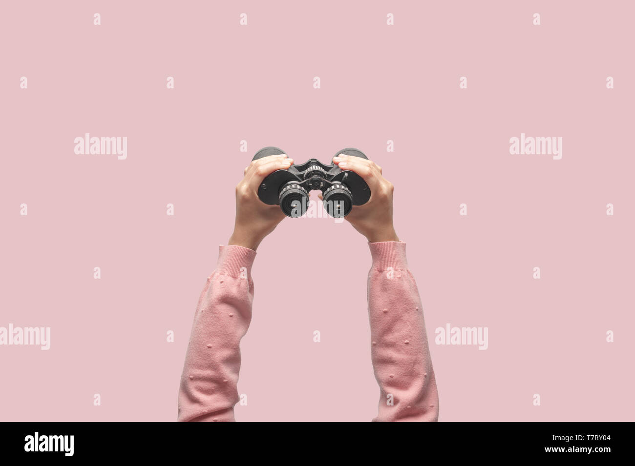 Woman with binoculars on retro pink background, looking through binoculars, journey, find and search concept. Stock Photo