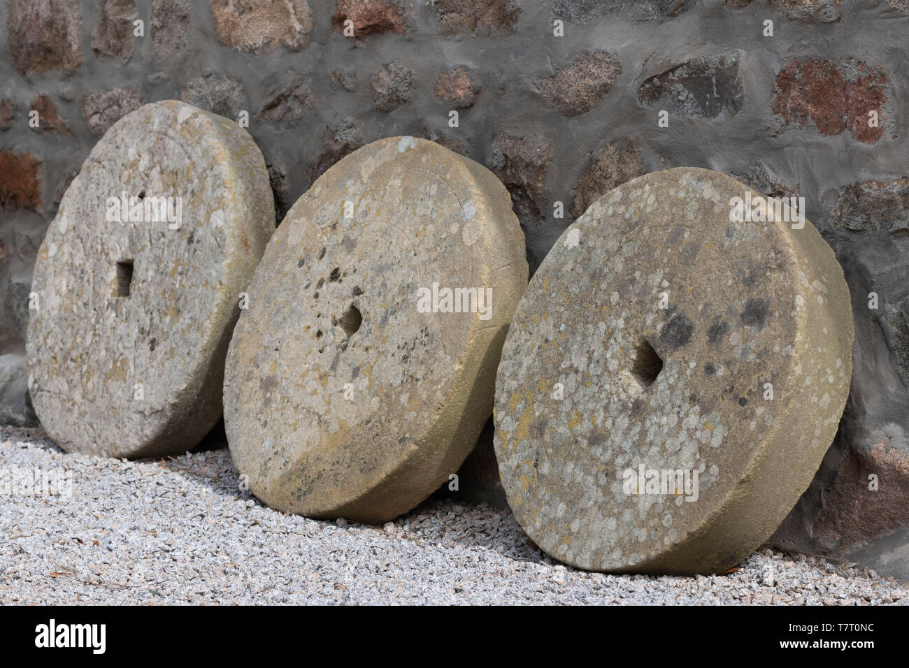 Three Millstones Propped Up Against a Stone Wall Stock Photo
