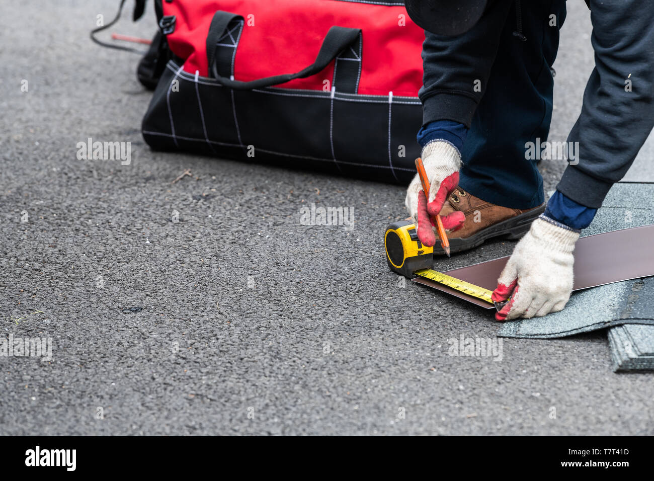Closeup of construction man measuring roof shingles with tape on asphalt ground driveway street