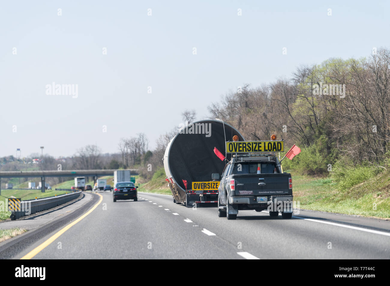 Woodstock, USA - April 18, 2018: Hauler truck trailer hauling oversize load of concrete pipe tube on interstate highway road in Virginia with yellow w Stock Photo