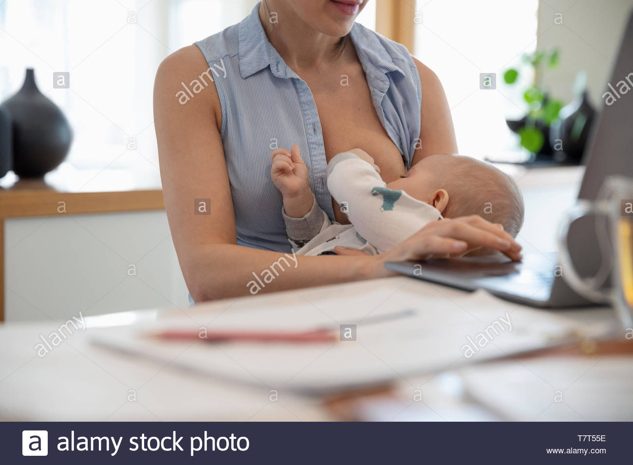 Mother breastfeeding while working from home Stock Photo