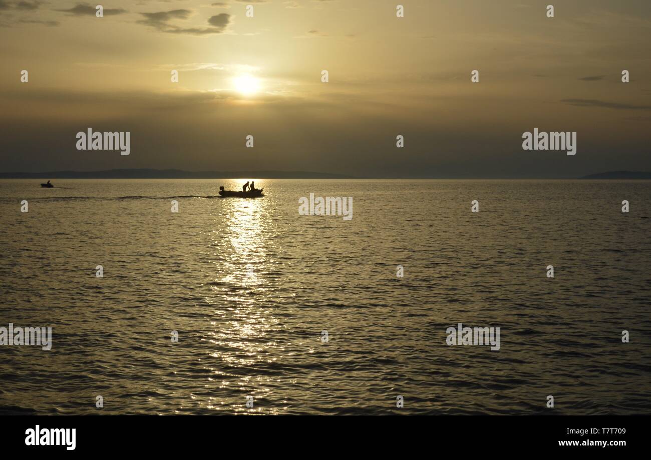 Fishing boat in sunset, caught in sun beam Stock Photo