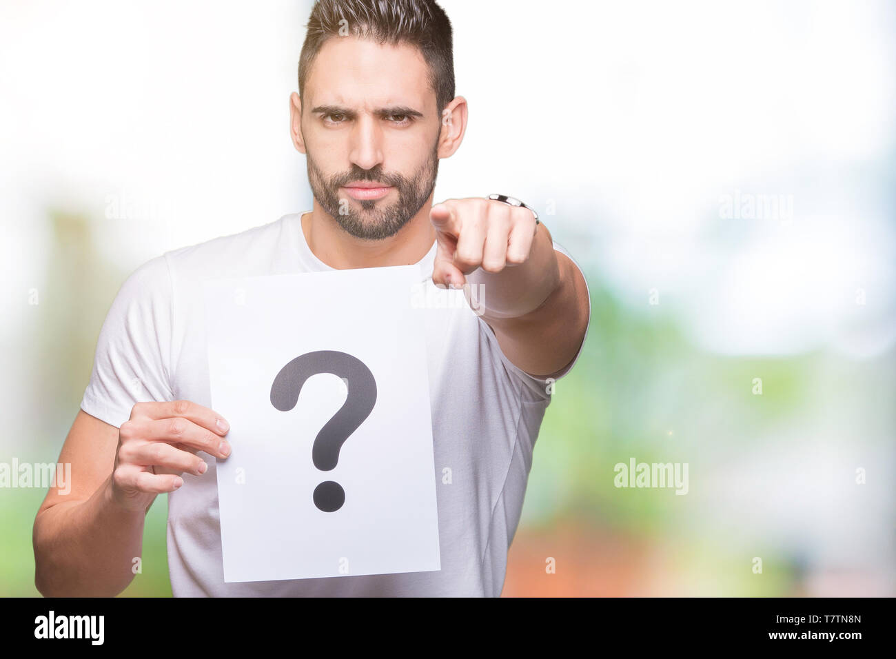 Handsome young man holding paper with question mark over isolated ...