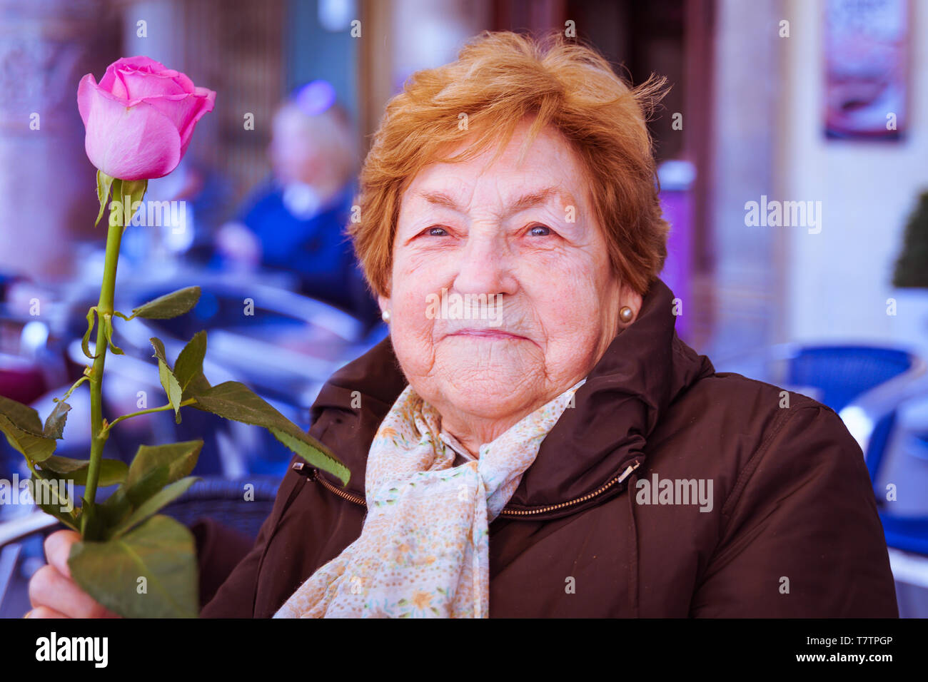 Smiling old woman with a pink rose Stock Photo